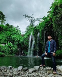 Man sitting by plants against trees