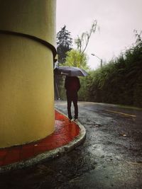 Rear view of man walking on wet rainy day