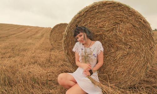 Portrait of woman sitting against hay bale