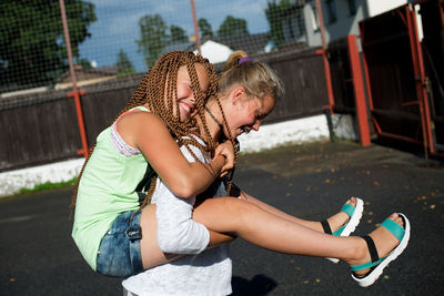 Side view of girl piggybacking happy female friend at playground