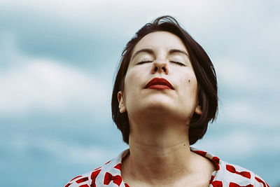 Young woman with eyes closed against sky