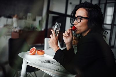 Woman drinking wine and eating fruit at table