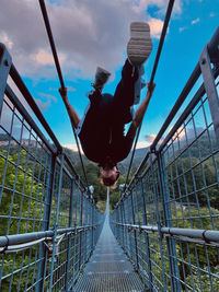 Man standing on footbridge against sky