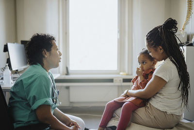 Woman carrying ill daughter discussing with pediatric in clinic