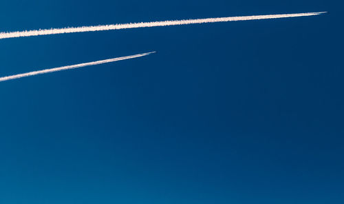 Low angle view of vapor trails against clear blue sky