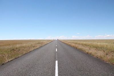 Empty road amidst field against blue sky