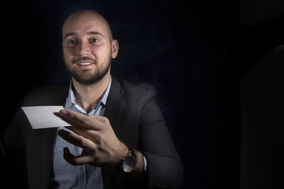 Mid adult man holding blank business card against black background