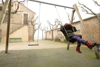 Young girl sheltered in an abandoned swing set with hood, unrecognisable.