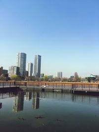 Bridge over river by buildings against clear blue sky