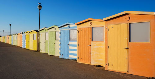 Beach huts by buildings against clear blue sky