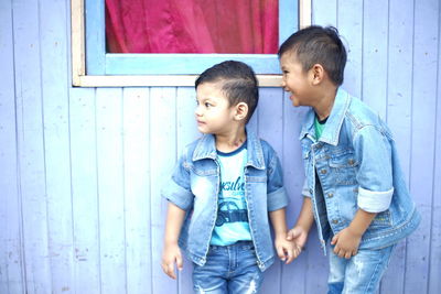 Happy siblings standing by wooden wall