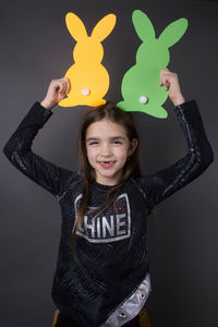 Portrait of smiling girl holding paper eater bunny against gray background