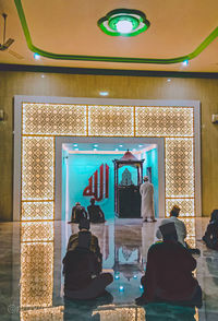 Rear view of people standing against illuminated building