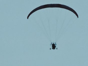 Low angle view of silhouette person paragliding against clear blue sky