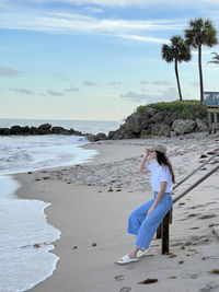 Rear view of woman standing at beach against sky