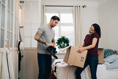 Man removing shoes from box while woman talking on phone at new home