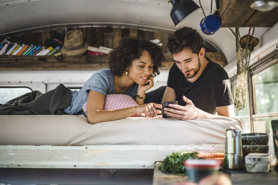 Young couple sharing smart phone while lying on bed in caravan