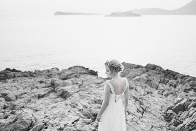 Rear view of woman standing on rock against sea