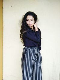 Portrait of young woman standing against wall