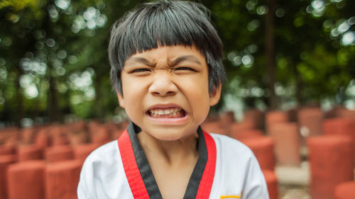 Close-up portrait of boy clenching teeth against trees