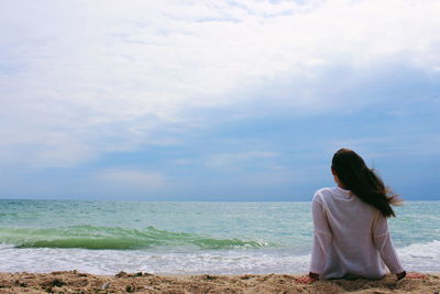 Rear view of woman relaxing at beach against sky