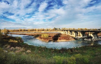 Arch bridge over river against cloudy sky