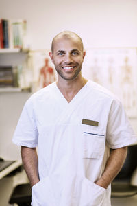Portrait of smiling orthopedic surgeon standing with hands in pockets in clinic