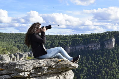 Side view of woman photographing on rock