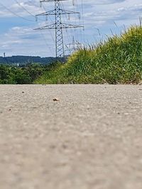 Surface level of road by electricity pylon against sky