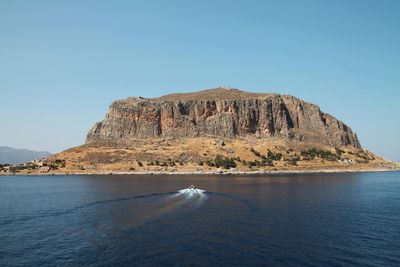 Rocky mountain by sea against clear sky