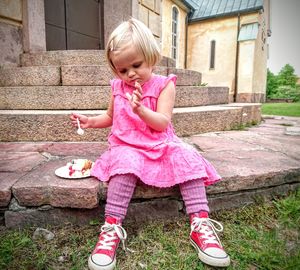 Full length of cute girl eating sweet food on steps against house