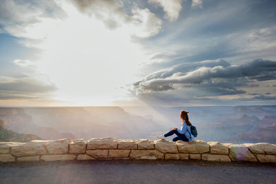 Full length of woman sitting on retaining wall against sky