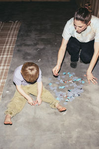 High angle view of boy solving puzzle with mother while sitting on floor at home