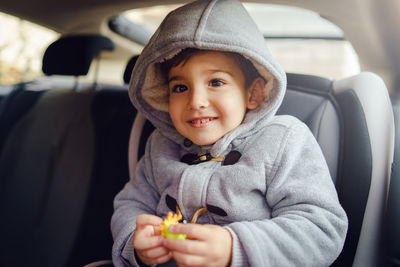 Cute boy wearing hood sitting at car