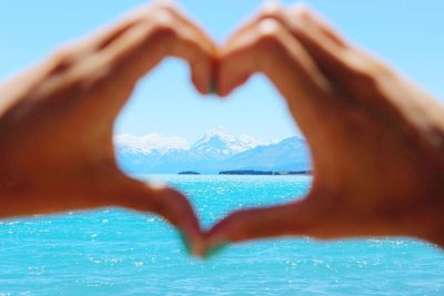 Cropped hands of woman making heart shape in front of sea