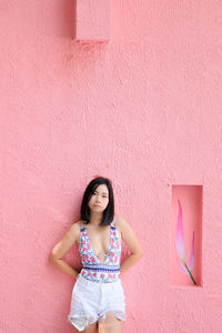 Portrait of woman standing against pink wall