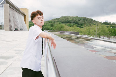 Side view of man standing by railing against sky