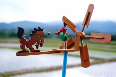 Close-up of figurine on wooden pinwheel toy with agricultural field