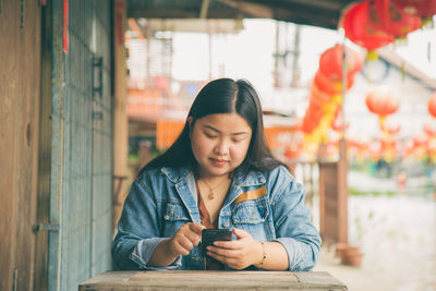 An asian woman in a jeans jacket sitting while using an application on her mobile phone 
