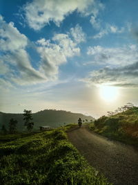 Road amidst field against sky during sunset