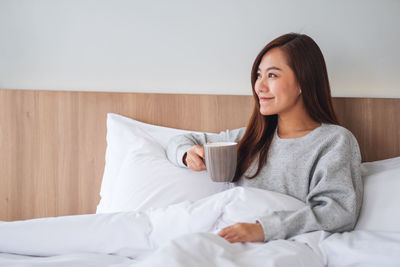 Portrait of young woman sitting on bed at home