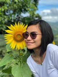 Close-up of smiling young woman wearing sunglasses standing by sunflower