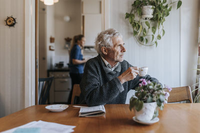 Thoughtful senior man holding tea cup while sitting at dining table in home