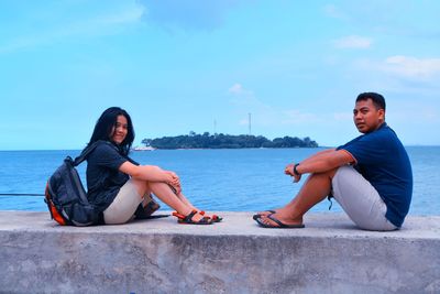 Side view portrait of couple sitting on railing against sea