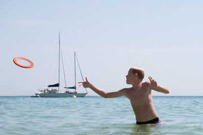 Boy playing in sea against clear sky