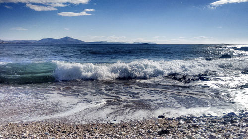 Waves rushing towards shore against sky