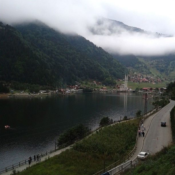 mountain, water, mountain range, sky, river, built structure, architecture, transportation, tree, lake, building exterior, scenics, nature, cloud - sky, high angle view, beauty in nature, tranquility, tranquil scene, mode of transport, landscape