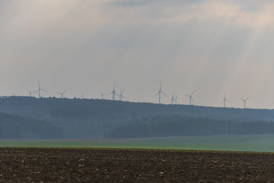 Wind turbines on field against sky