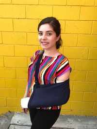 Portrait of smiling young woman with fracture hand standing against wall