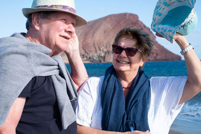 Senior couple smiling while standing against sea during sunny day